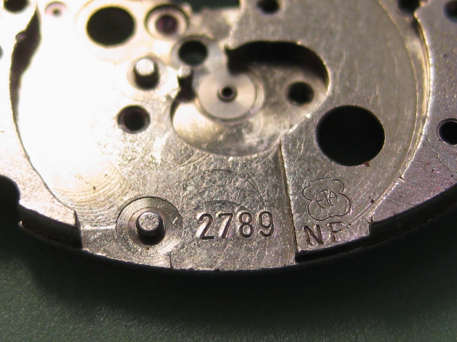 Primer plano de la placa principal de un movimiento de reloj automático vintage ETA 2789-NF, mostrando el número de calibre grabado "2789", marca ETA con el logo de la flor suiza, código "NF" y varios orificios para pivotes y rubíes visibles.